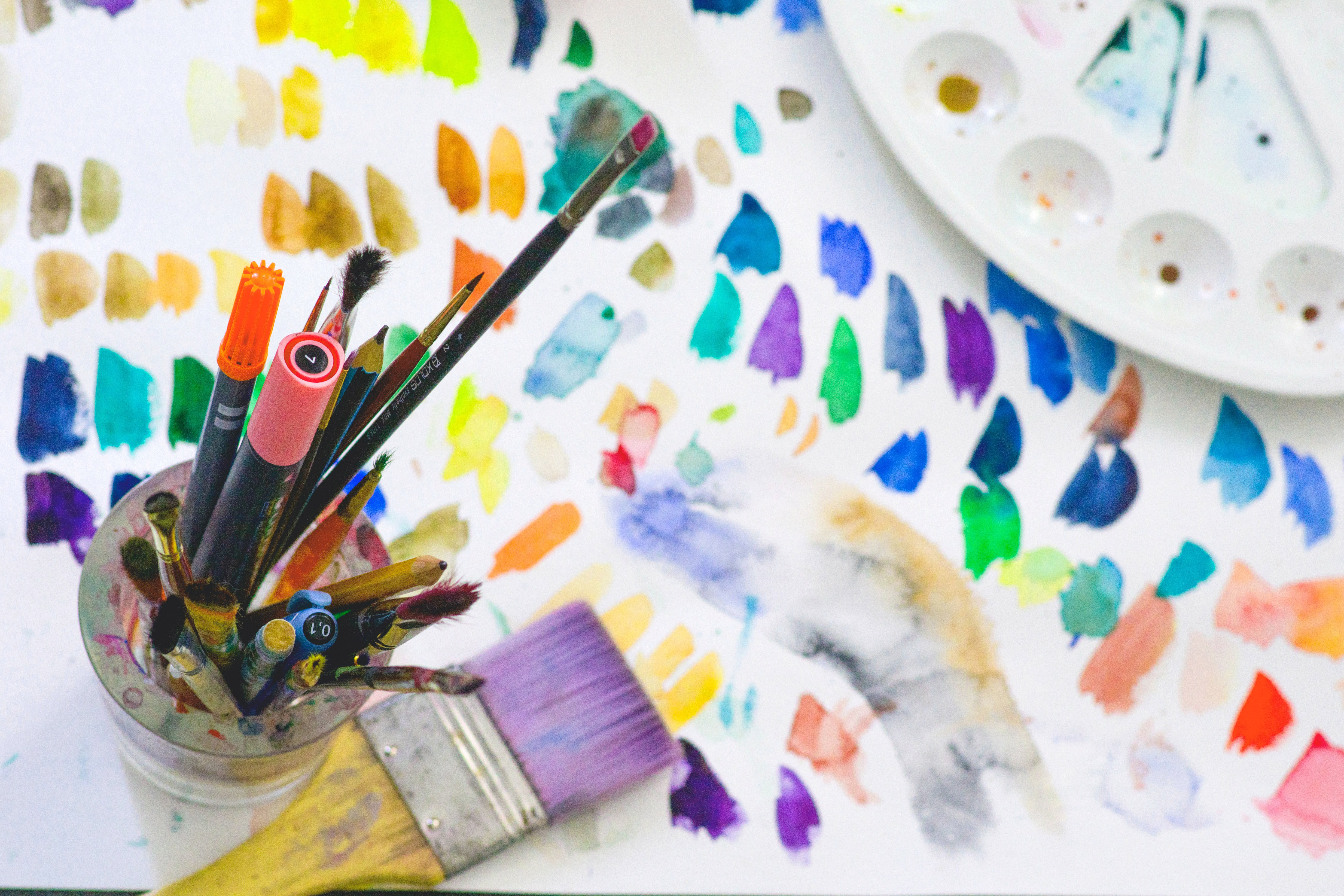 multicoloured page of paint colour tests with paintbrush and pot of pens