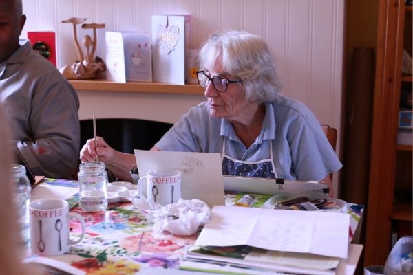 Marion painting; she is inside a house and the table is filled with painting supplies.