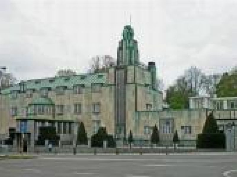 big stone building with many windows, green roof and cloudy sky